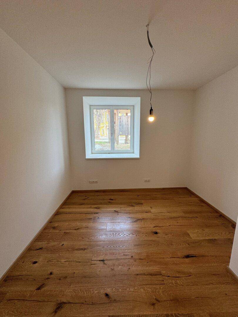 Gemütliches Schlafzimmer mit Holzdielenboden und einem Fenster, das den Raum mit Tageslicht erhellt.