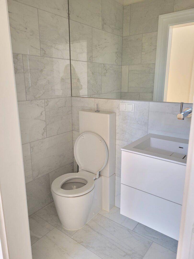 Modernes WC mit Wand-WC, Waschbecken und großformatigen Marmorfliesen, ergänzt durch einen großen Spiegel.