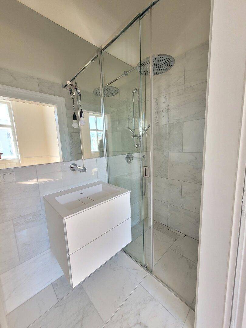 Helles Badezimmer mit moderner Glasdusche, Regendusche und eleganten Marmorfliesen, die den Raum aufhellen.