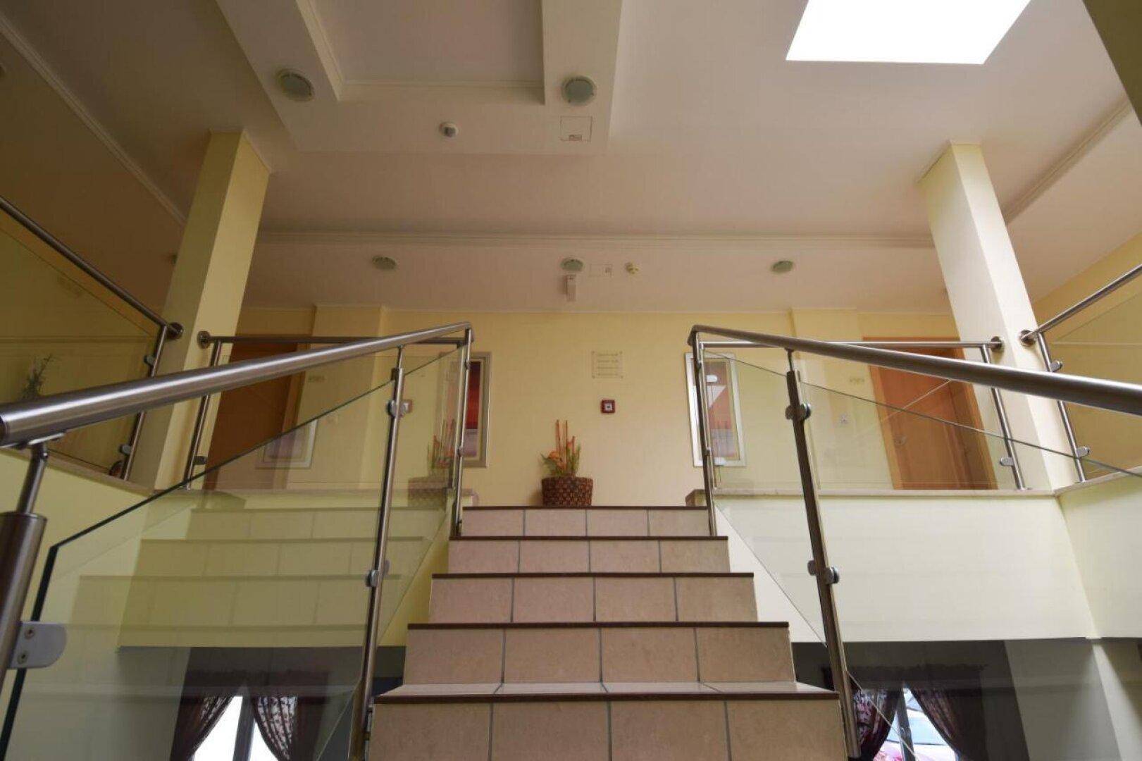 Elegante Treppe mit Glas- und Metallgeländer in einem hellen Eingangsbereich mit beigen Wänden.