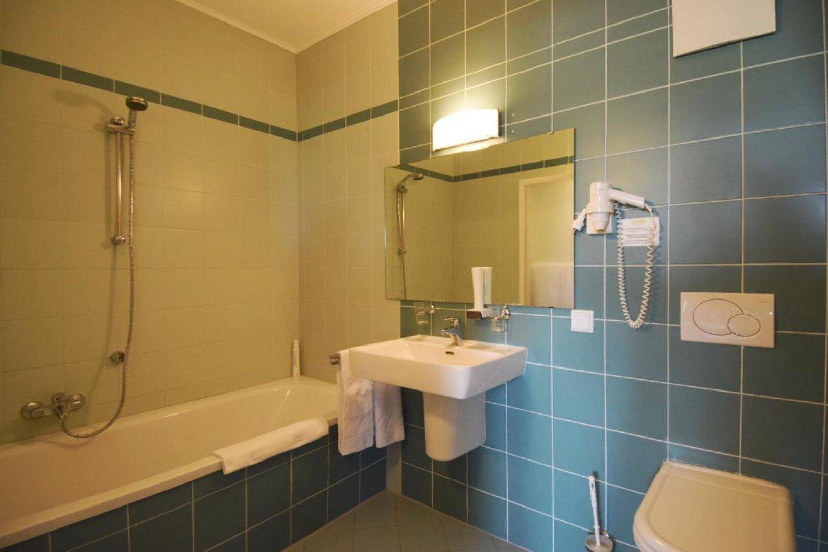 Badezimmer mit Badewanne, Standwaschbecken und WC, gefliest in Türkis und Beige.