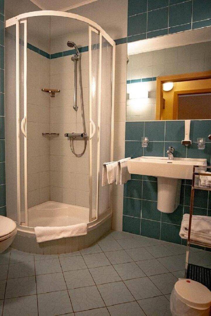 Badezimmer mit Eckduschkabine, Standwaschbecken und WC, gefliest in Türkis und Hellblau.