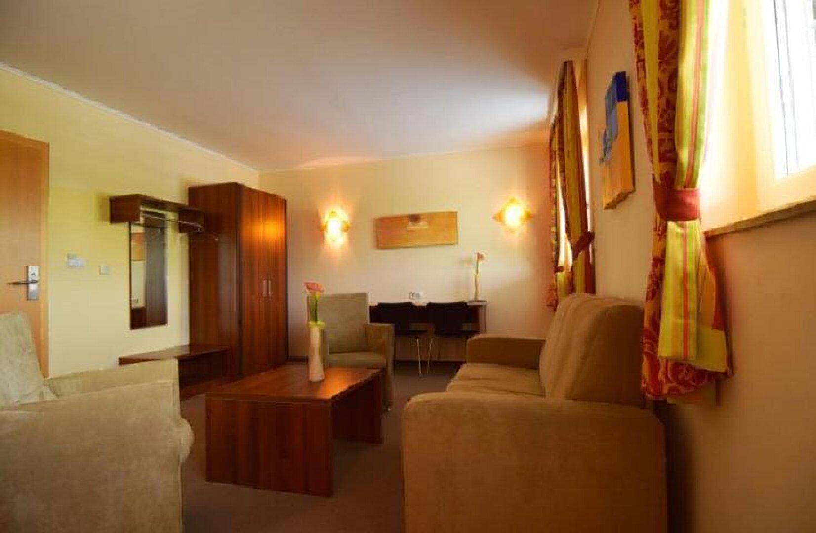 Gemütliches Wohnzimmer mit beigem Sofa, Sessel, Couchtisch und einem Holzschrank.