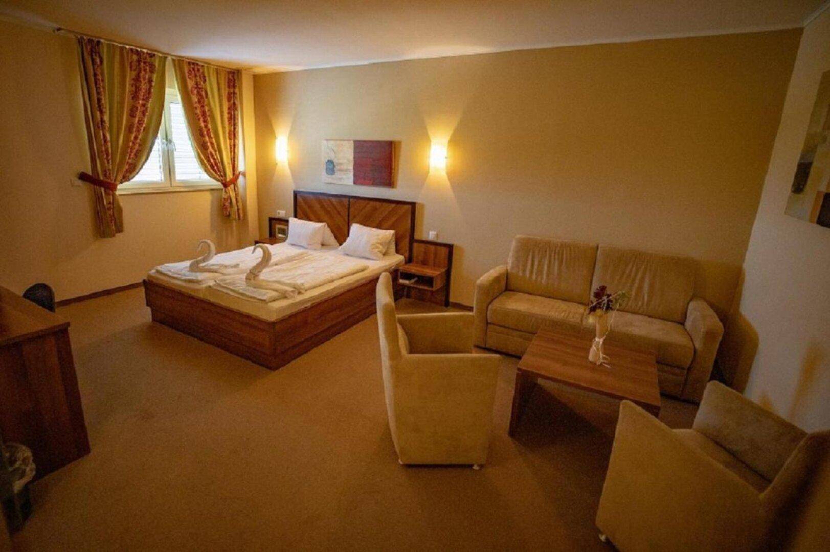 Geräumiges Schlafzimmer mit Doppelbett, beigem Sofa, Sessel und einem Couchtisch vor dem Fenster.