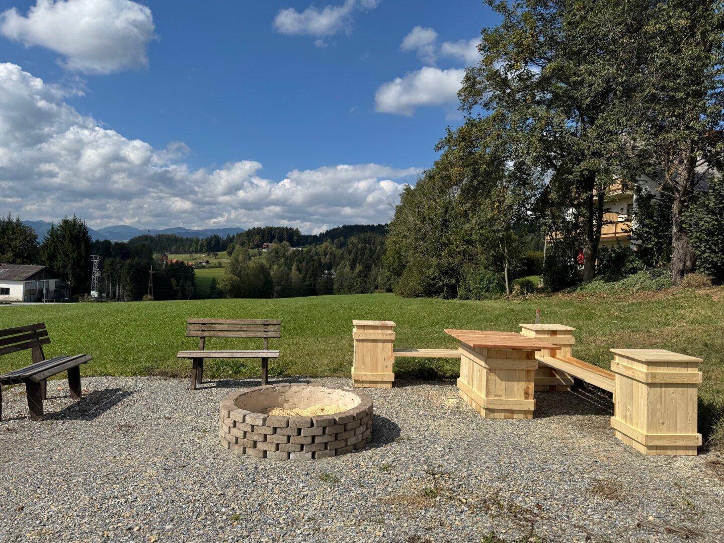 Idyllischer Außenbereich mit Feuerstelle und Holzbänken, umgeben von Natur.