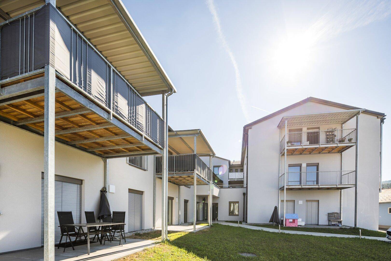 Mehrfamilienhaus mit Balkonen und Terrassen, umgeben von einer gepflegten Grünfläche unter strahlendem Sonnenschein.