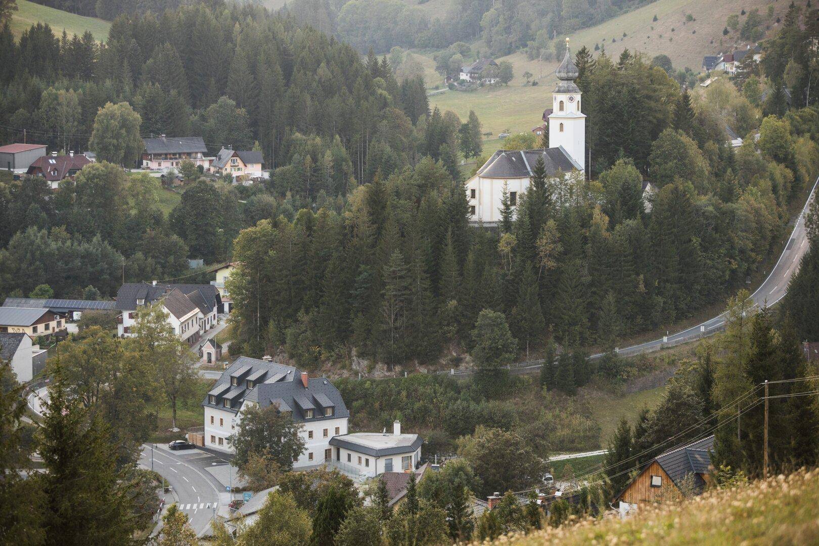 Malerisches Dorf in einer grünen Hügellandschaft mit Kirche und traditionellen Gebäuden.