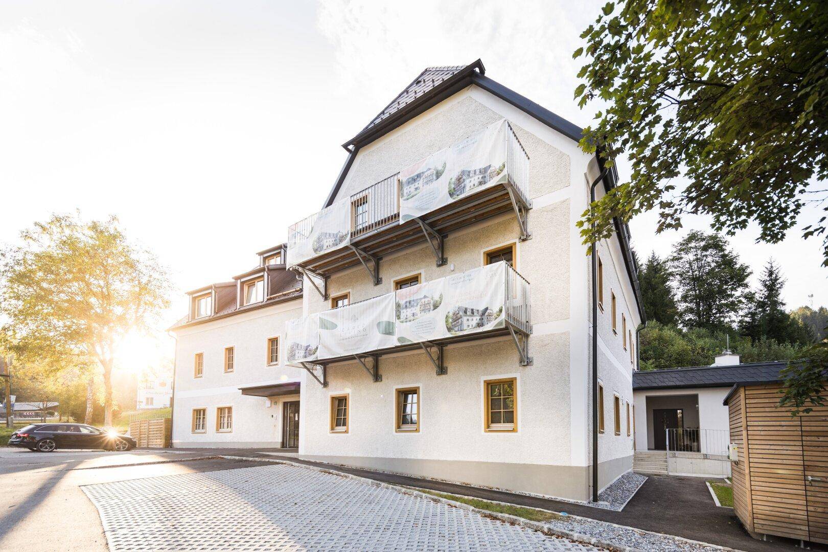 Moderne Gebäudefassade mit Balkonen und gepflegter Außenanlage unter strahlendem Sonnenschein.