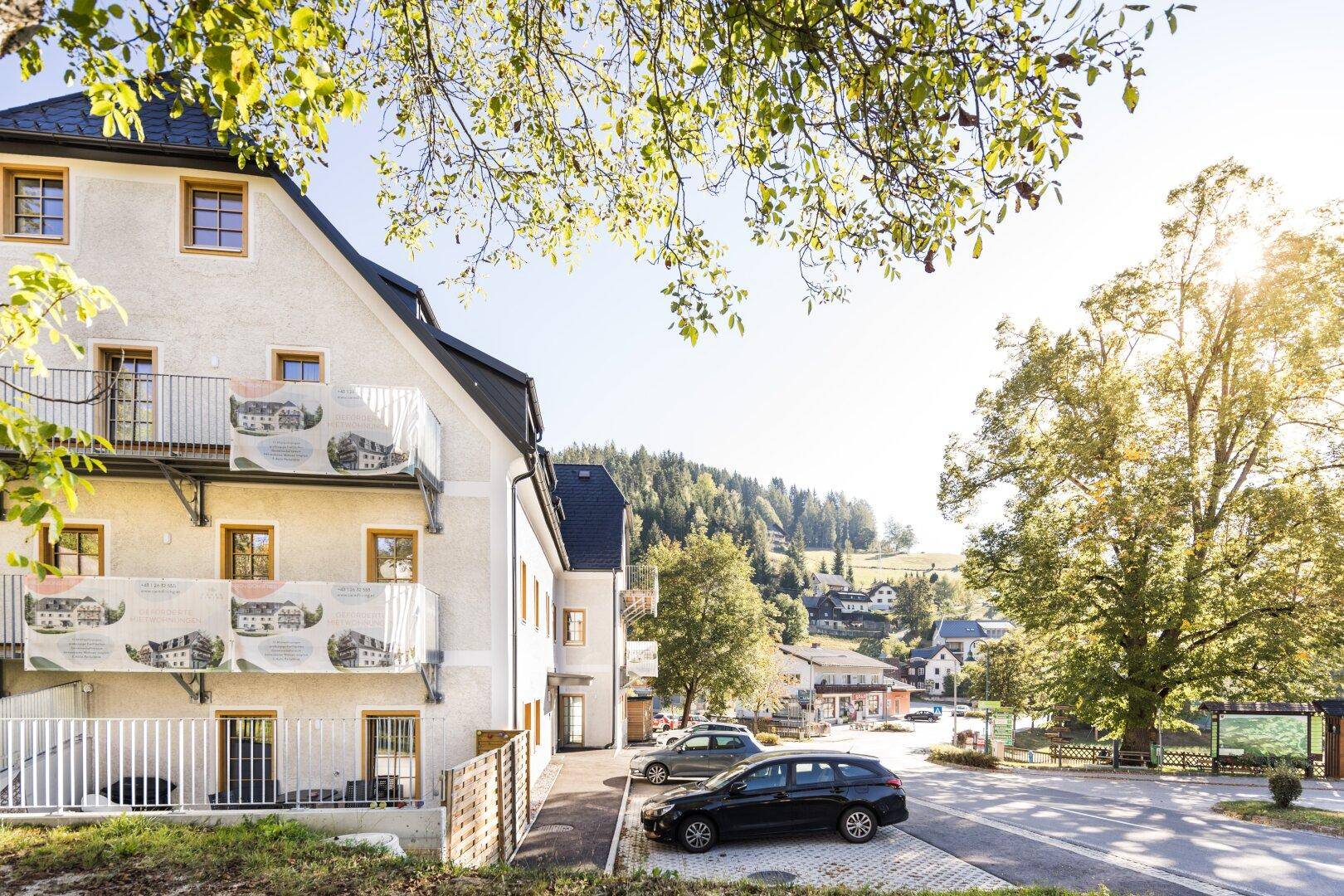 Attraktives Mehrfamilienhaus mit Balkonen und Parkplätzen in sonniger ländlicher Umgebung.