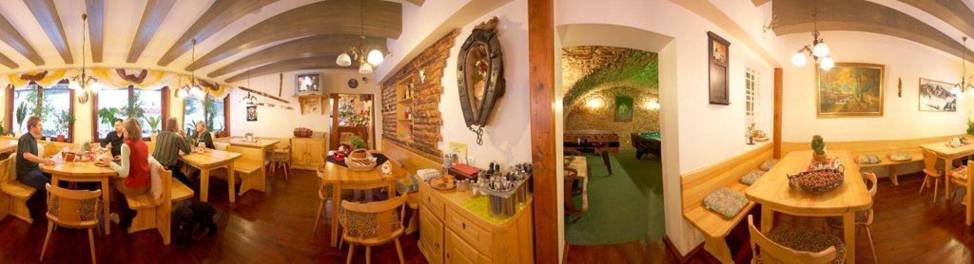 Weitläufiger Restaurantbereich mit rustikalen Holzmöbeln, Bar und Zugang zu einem Spielzimmer im Keller.