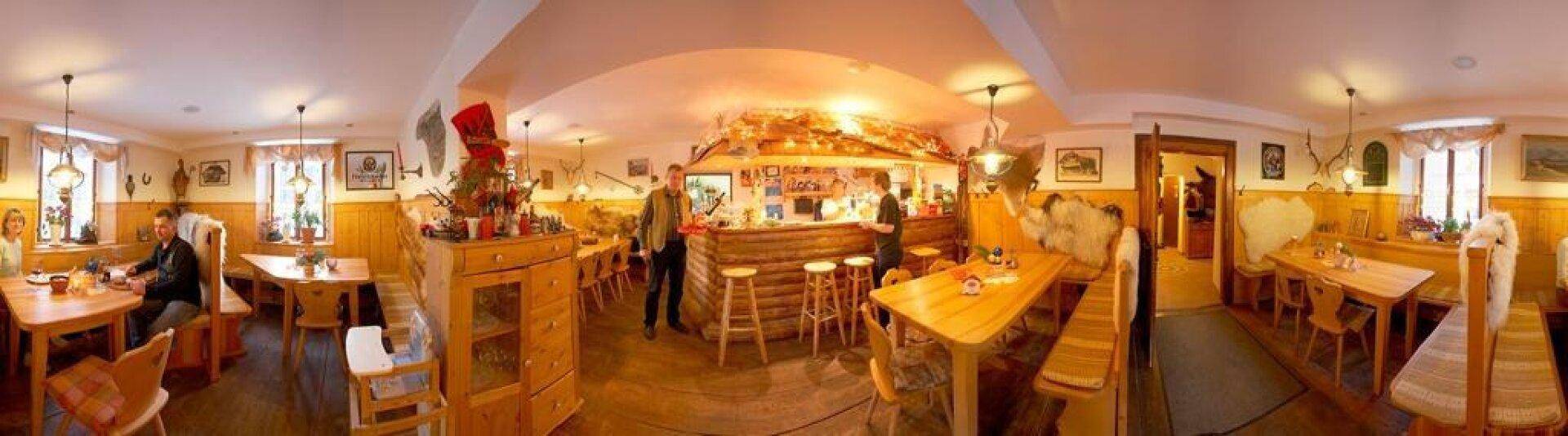 Rustikaler Restaurantbereich mit Holztischen, Bänken und einer Bar, beleuchtet von warmem Licht und traditioneller Einrichtung.