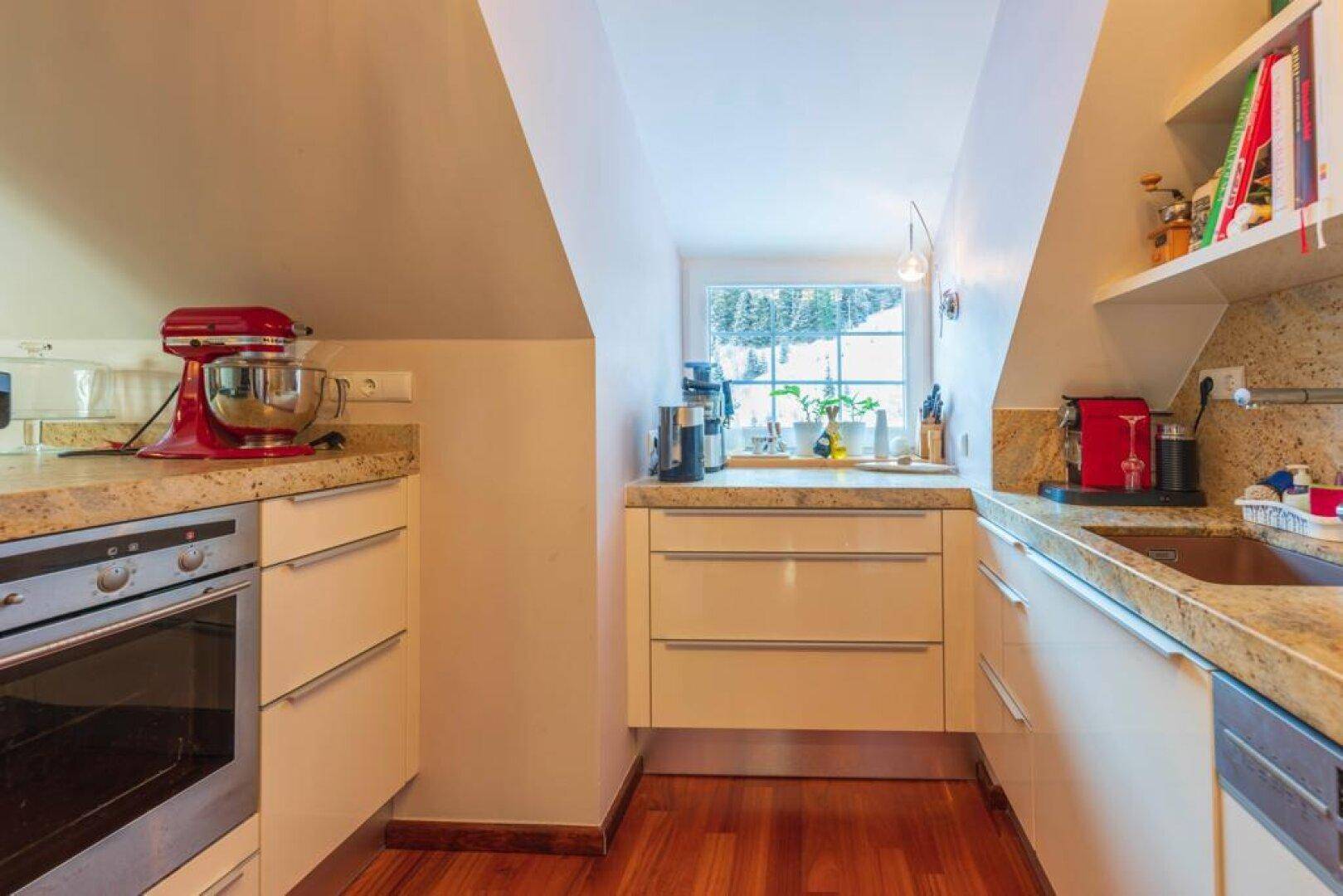 Helle Küche mit Dachschrägen, modernen weißen Schränken und Granitarbeitsplatten, mit Fensterblick.
