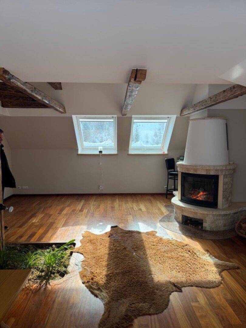 Heller Wohnbereich mit Holzboden, Kamin und Dachfenstern, die eine gemütliche Atmosphäre schaffen.