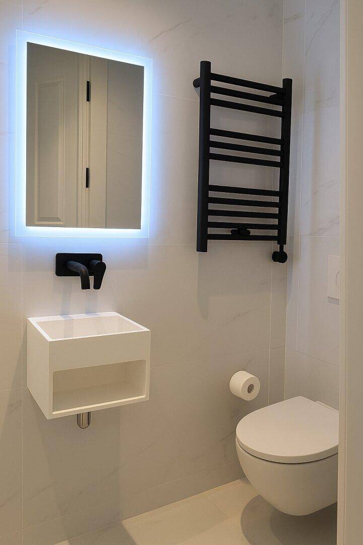 Modernes Badezimmer mit beleuchtetem Spiegel, schwarzer Armatur und beheiztem Handtuchhalter.