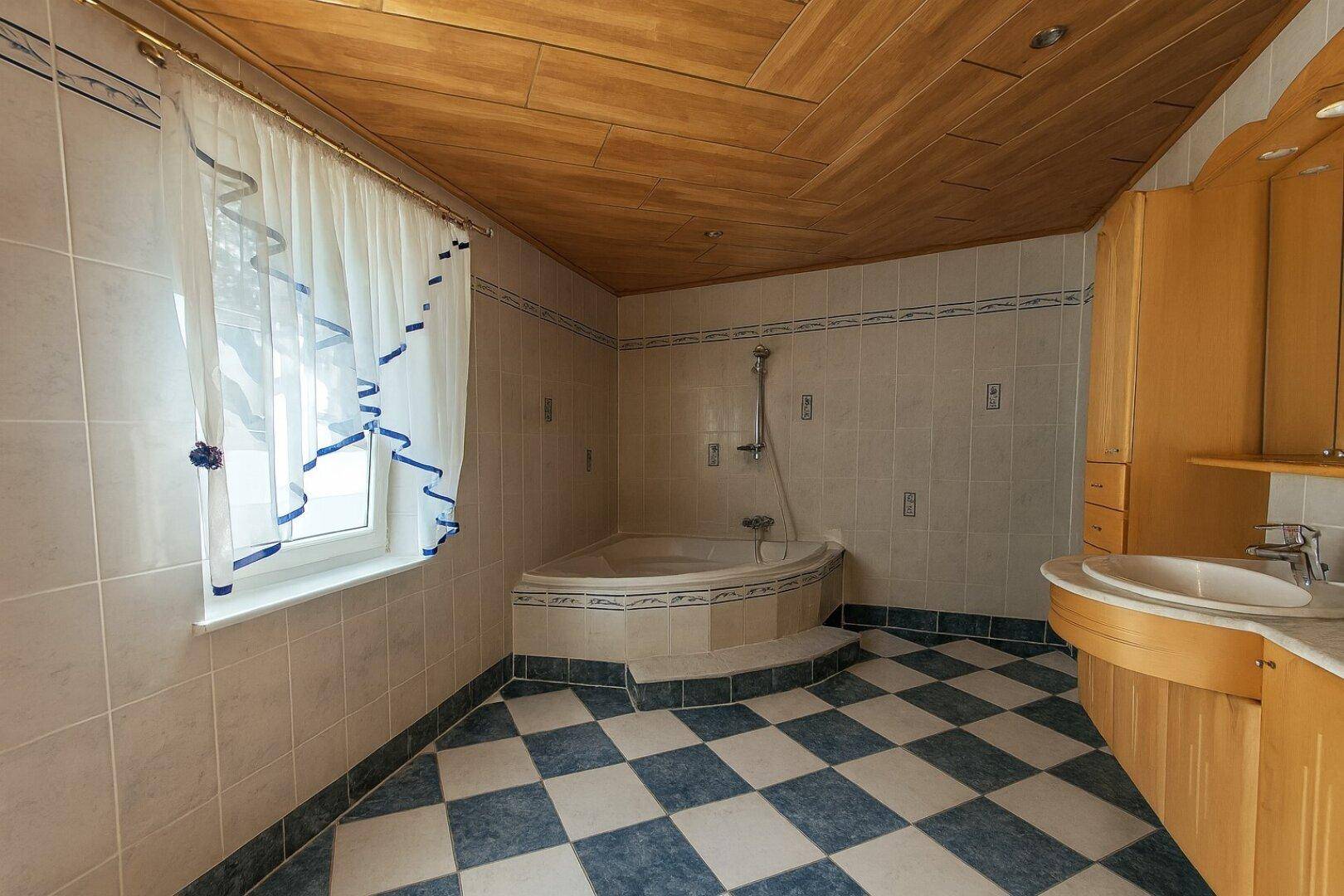 Geräumiges Badezimmer mit Eckbadewanne, Holzdecke und kariertem Fliesenboden.
