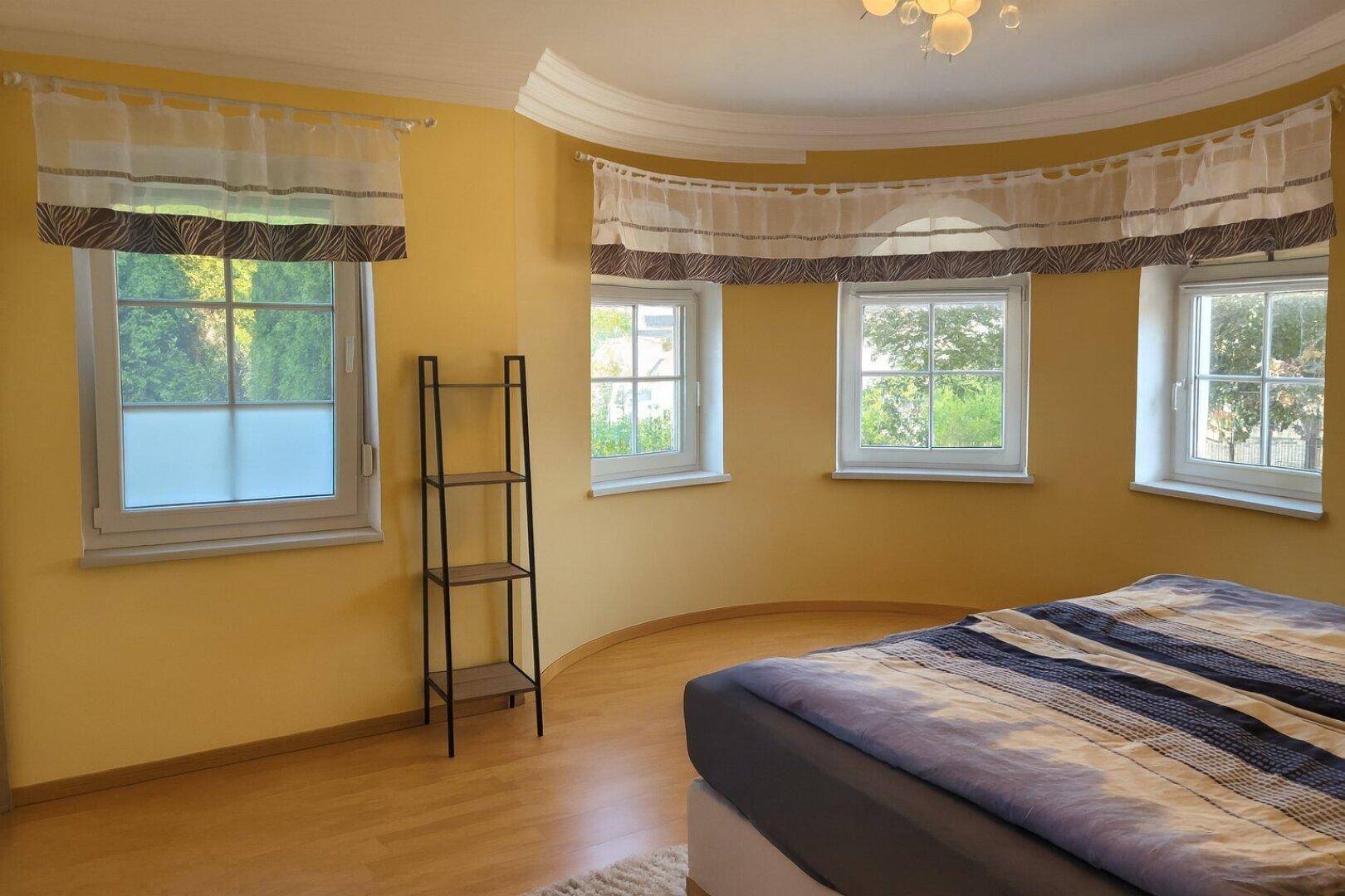 Helles Schlafzimmer im Turmzimmer mit mehreren Fenstern und Holzboden.