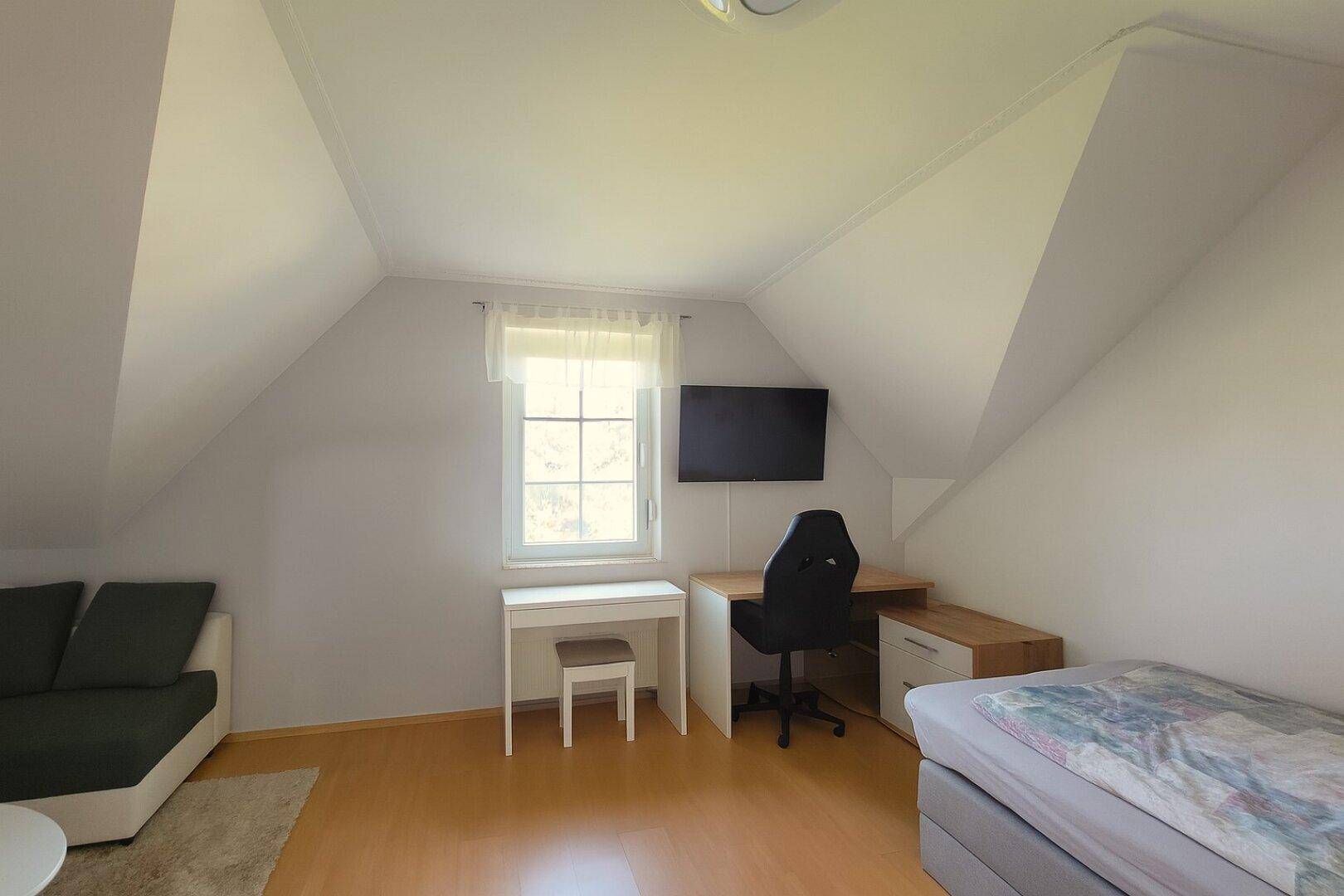 Dachgeschoss-Schlafzimmer mit schrägen Wänden, Holzboden und Fenster.