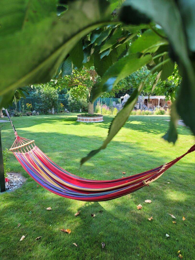 Bunte Hängematte im grünen Garten unter einem Baum an einem sonnigen Tag.