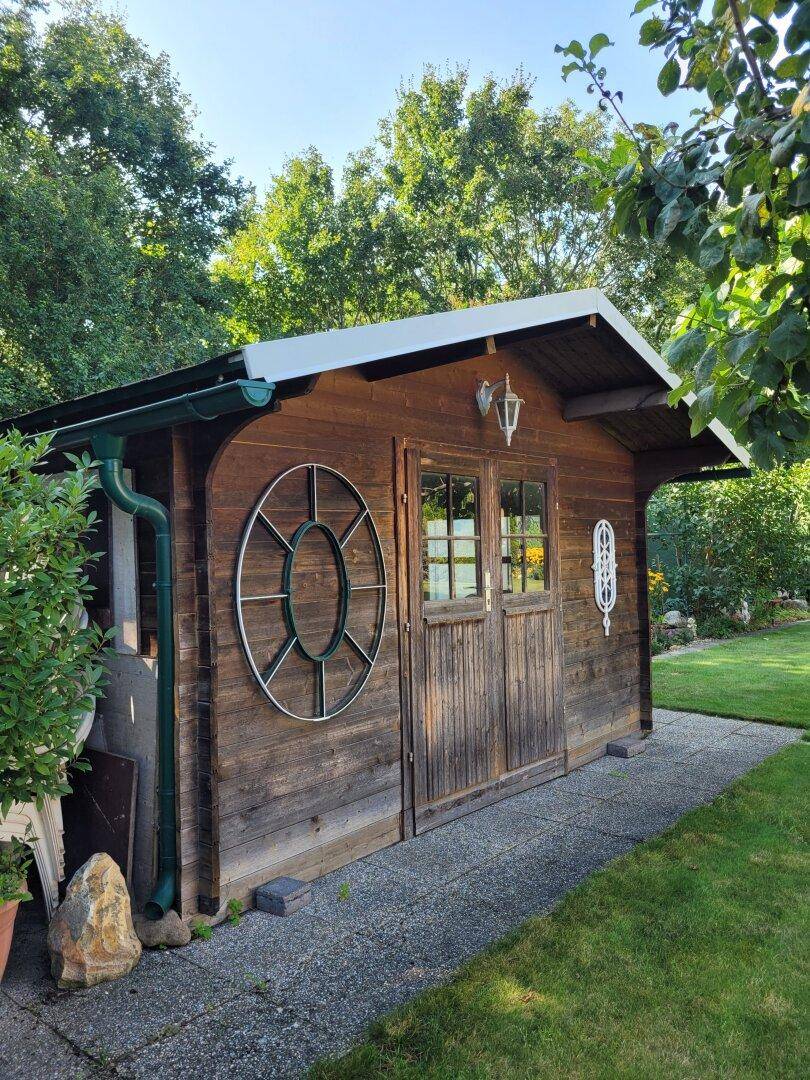 Rustikales Gartenhaus aus Holz mit dekorativen Fenstern und Vordach.