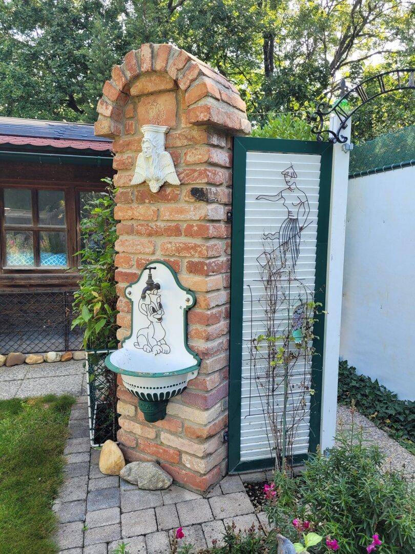 Dekorativer Gartenbrunnen aus Ziegelstein mit Wasserhahn und bemalter Tür.