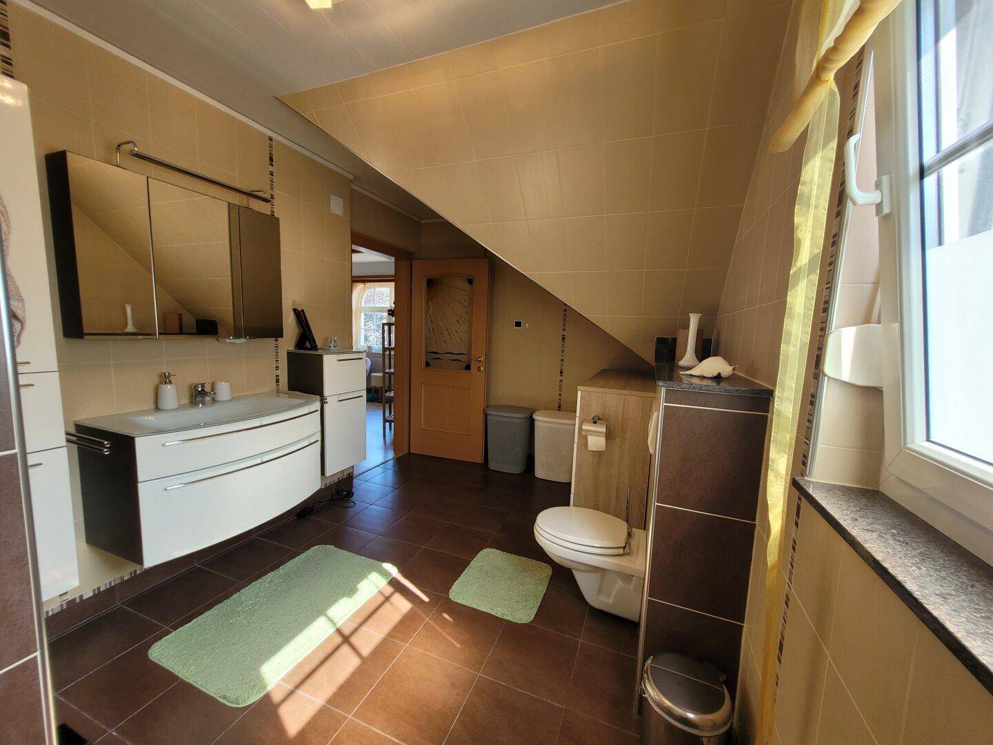 Modernes Badezimmer im Dachgeschoss mit Dachschräge, Doppelwaschbecken und braunen Fliesen.