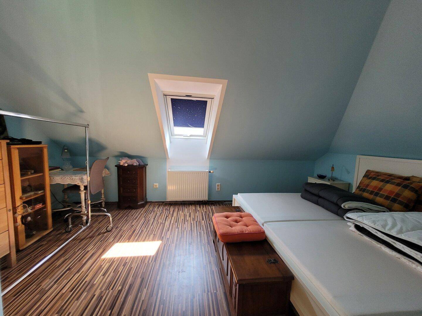 Helles Schlafzimmer im Dachgeschoss mit Dachfenster und Holzboden.