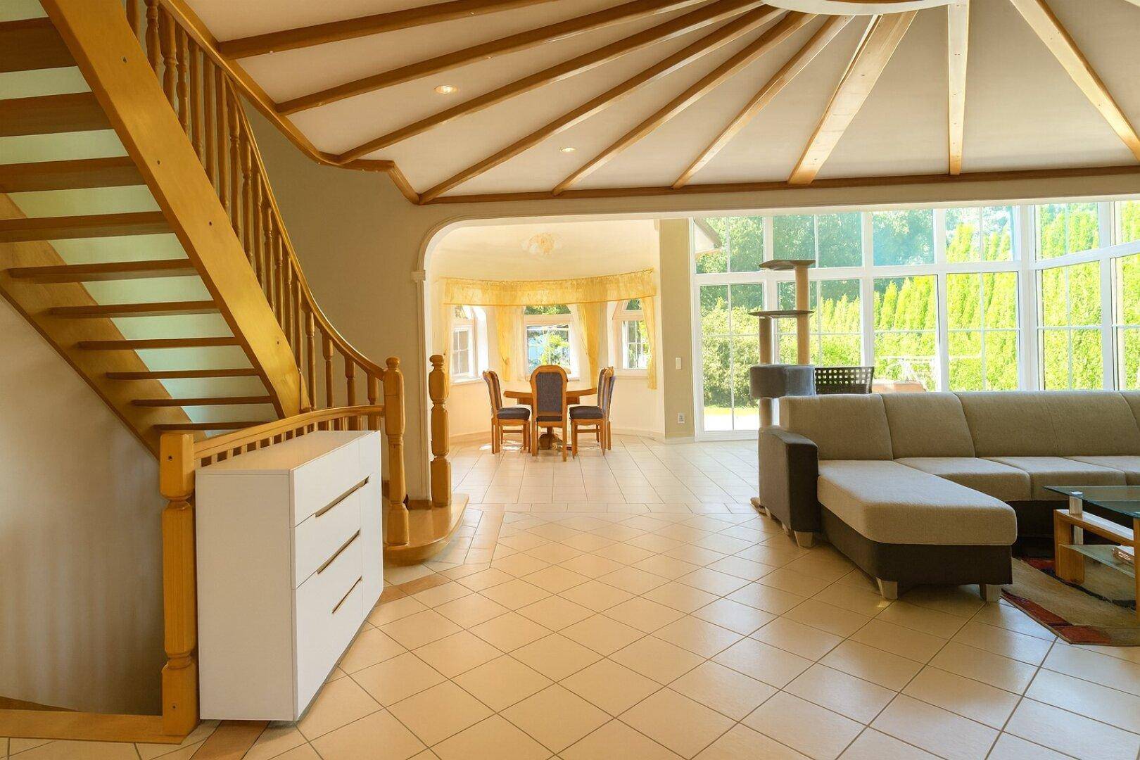 Heller Wohn- und Essbereich mit geschwungener Holztreppe und großen Fenstern zum Garten.
