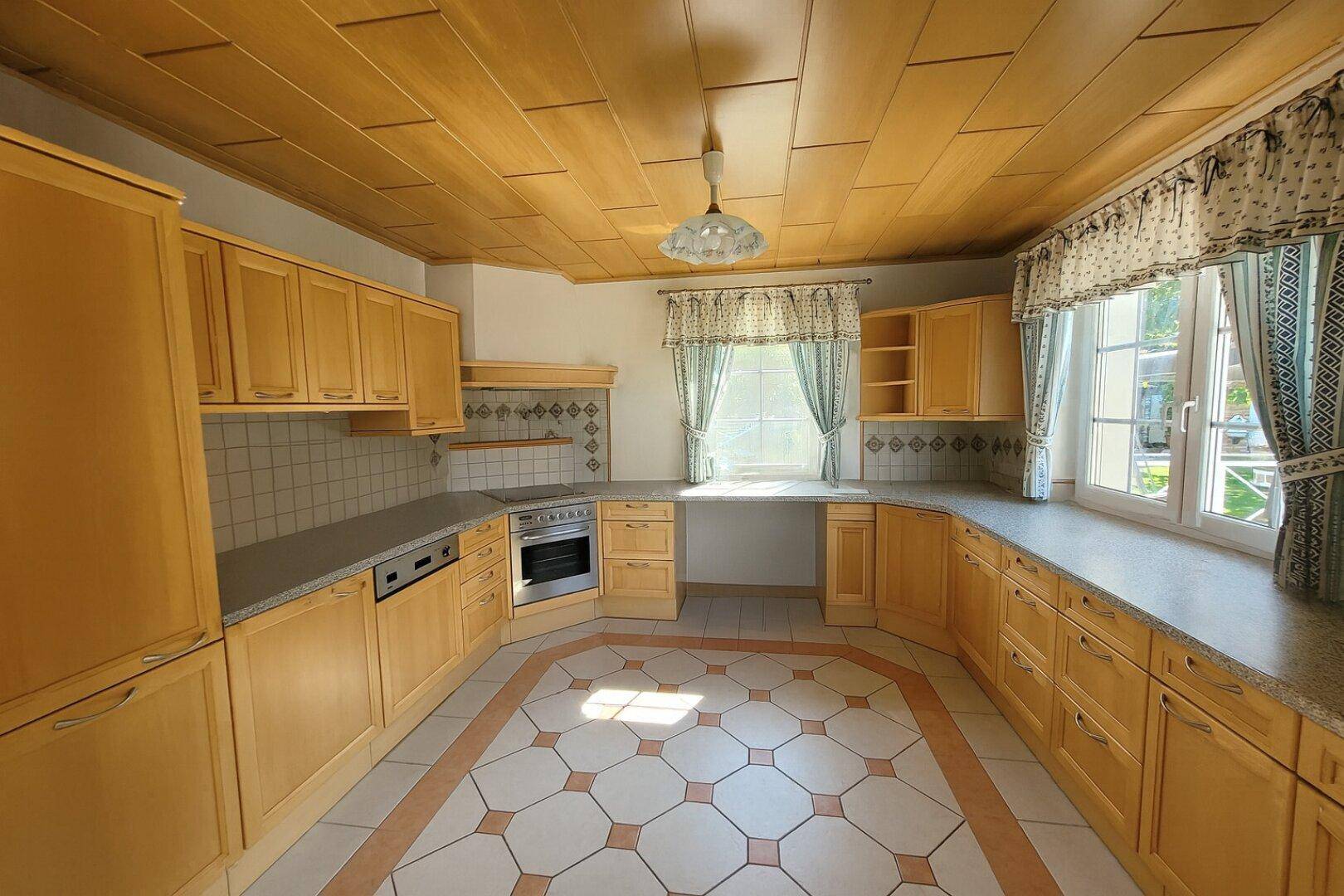 Traditionelle Holzküche mit gefliestem Boden und Fensterblick in den Garten.