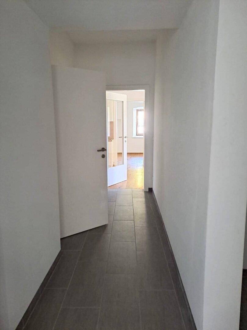 Heller Flur mit modernen grauen Fliesen und Zugang zu weiteren Zimmern mit Holzboden.