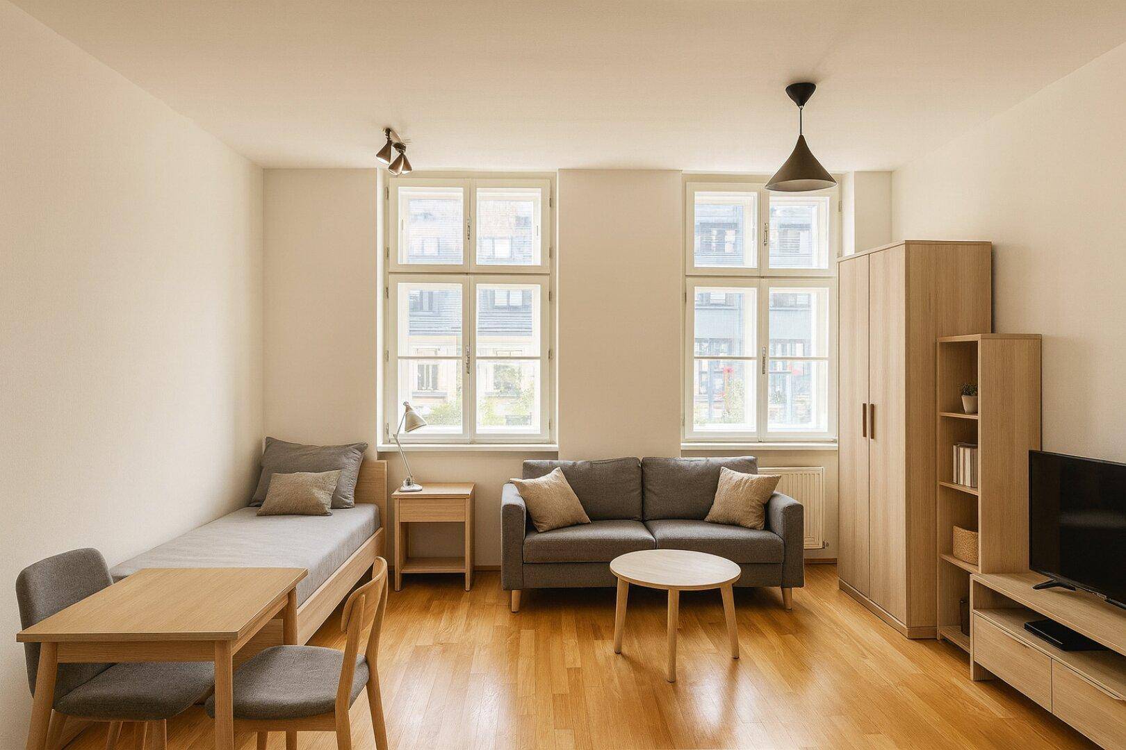 Gemütlicher Wohn- und Schlafbereich mit Holzboden, Sofa, Bett und Esstisch.