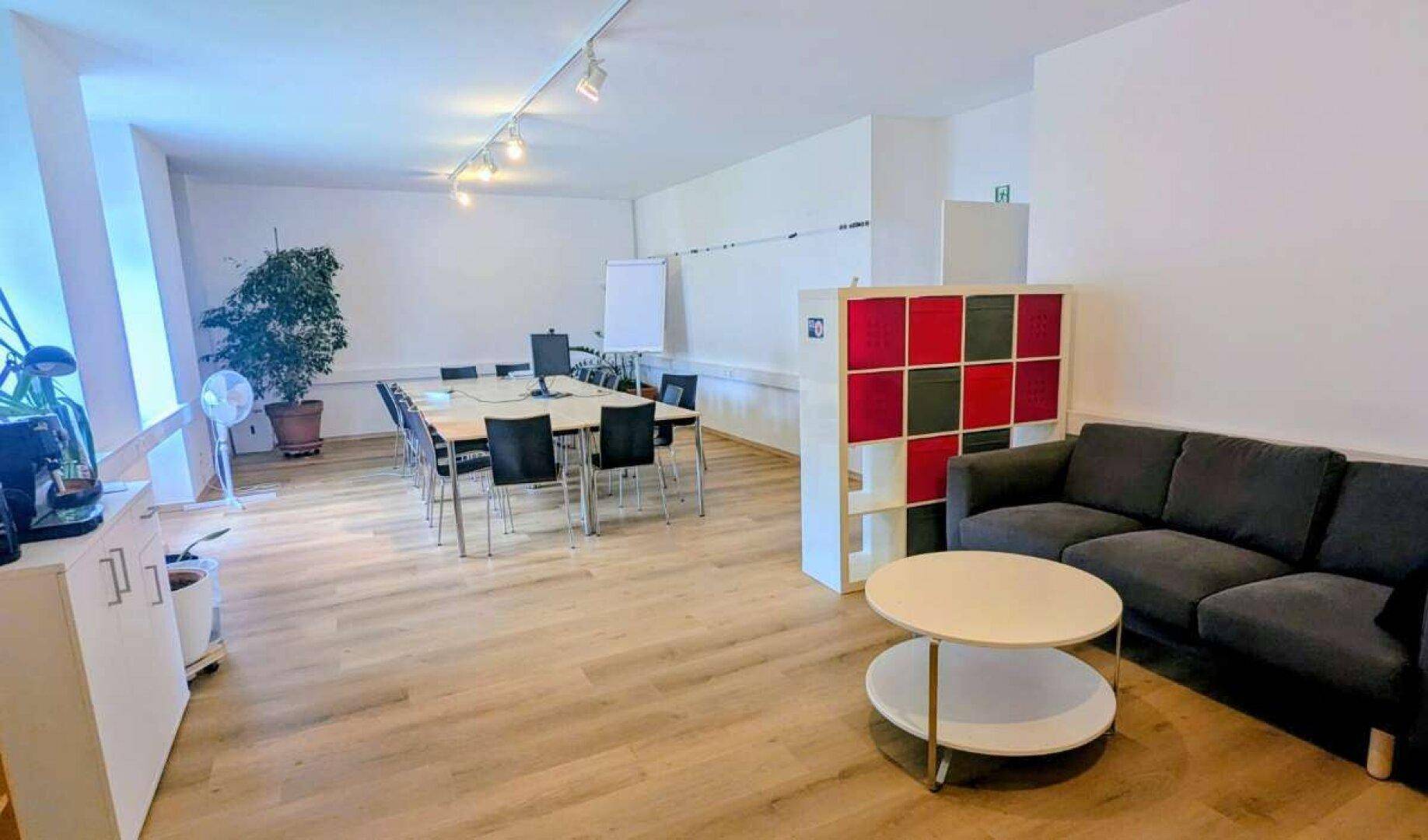 Geräumiger Bereich mit Besprechungstisch, Sofa und Regalsystem, ideal für Teamarbeit oder Pausen.