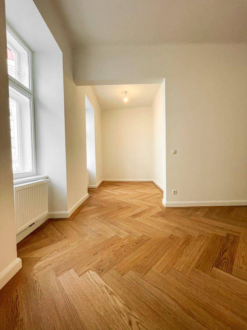 Helles Zimmer mit Fischgrätparkettboden und einem gemütlichen Alkovenbereich, ideal für verschiedene Nutzungen.