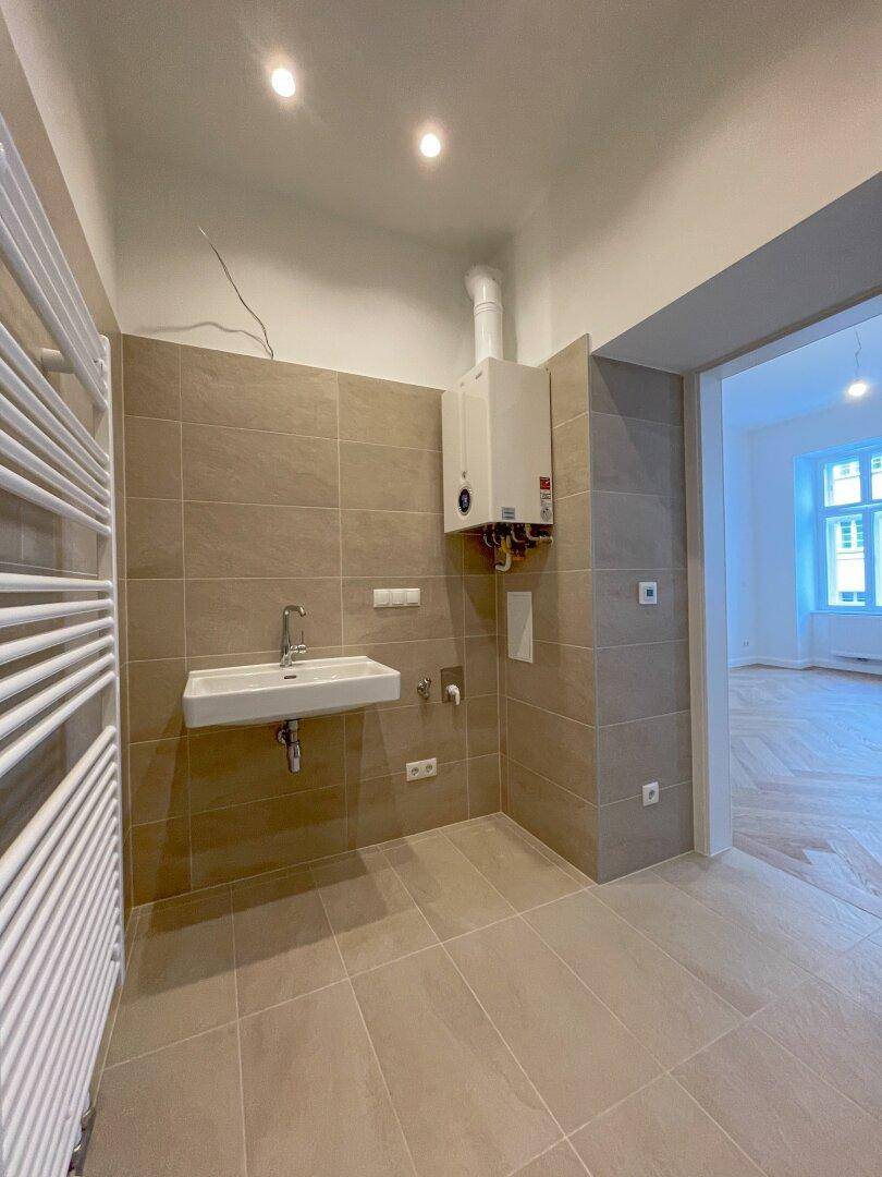 Modern gefliestes Badezimmer mit Waschbecken, Handtuchheizkörper und Warmwasserbereiter an der Wand.