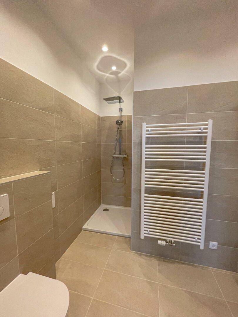 Modernes Badezimmer mit Regendusche, wandhängendem WC und praktischem Handtuchheizkörper, komplett gefliest.