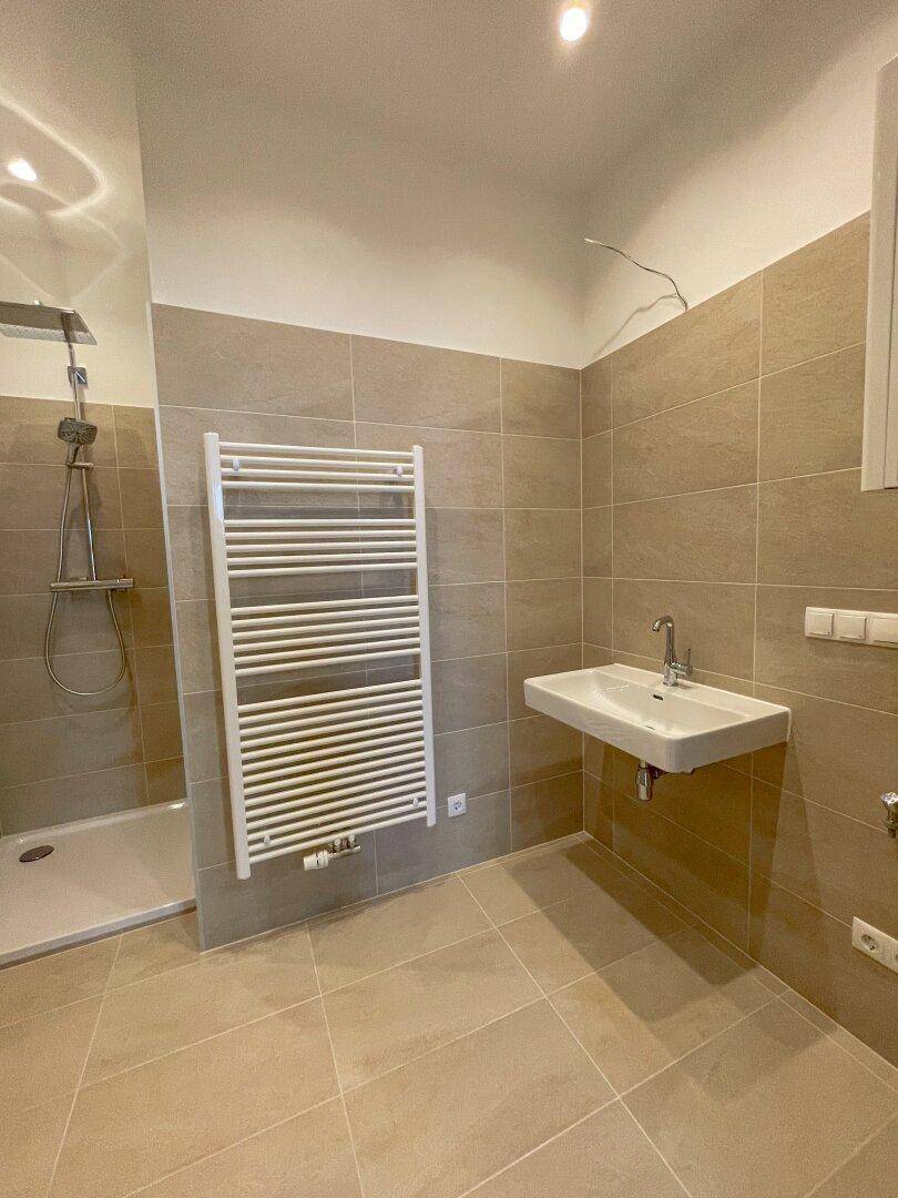 Gefliestes Badezimmer mit Waschbecken, Handtuchheizkörper und einem Duschbereich, der auf die Fertigstellung wartet.