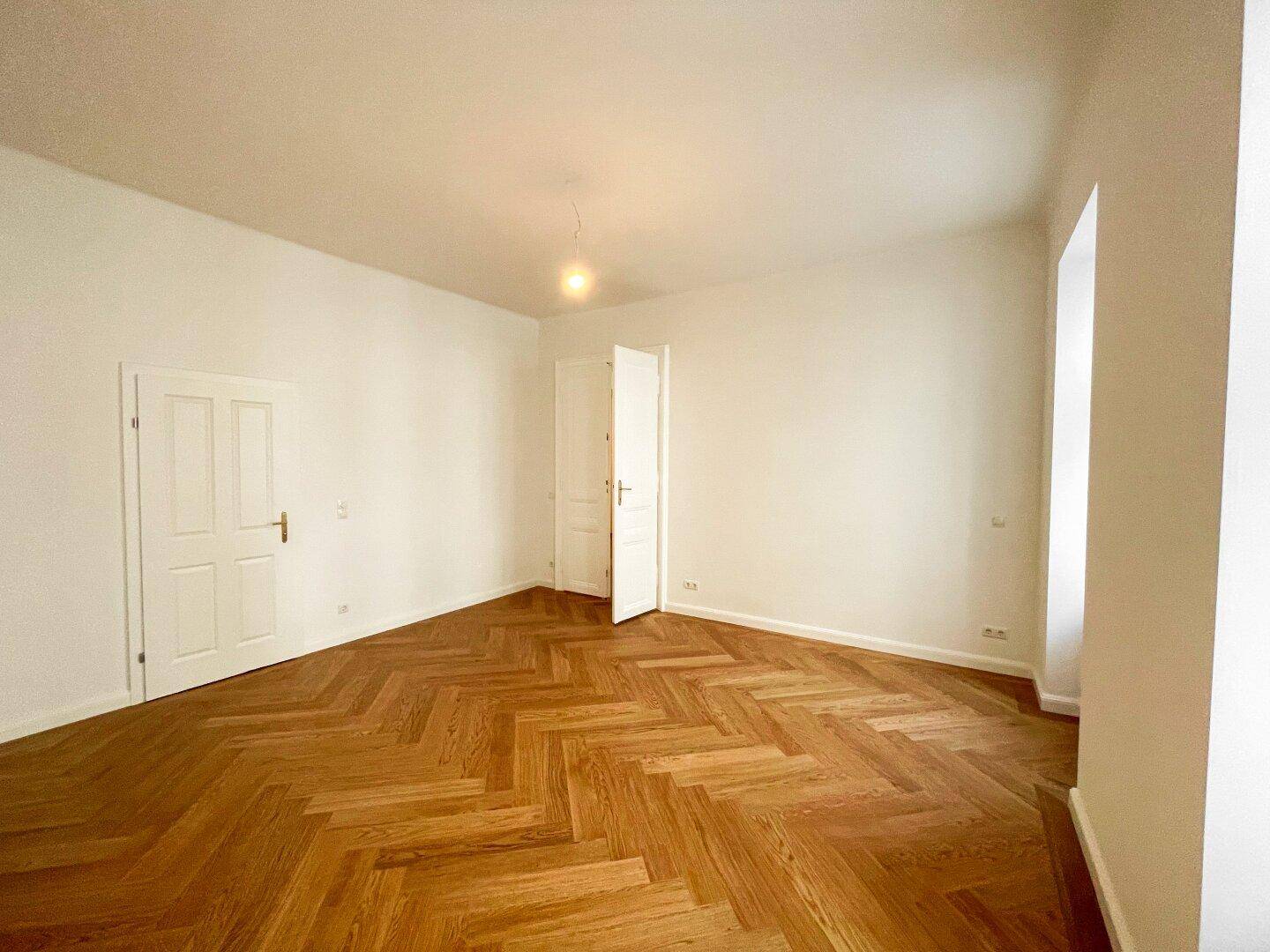 Geräumiges Zimmer mit elegantem Fischgrätparkettboden und zwei weißen Türen, die zu weiteren Räumen führen.