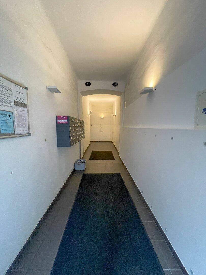 Eingangsbereich mit Briefkästen, Fliesenboden und Wandleuchten, der zu den Wohnungen führt.