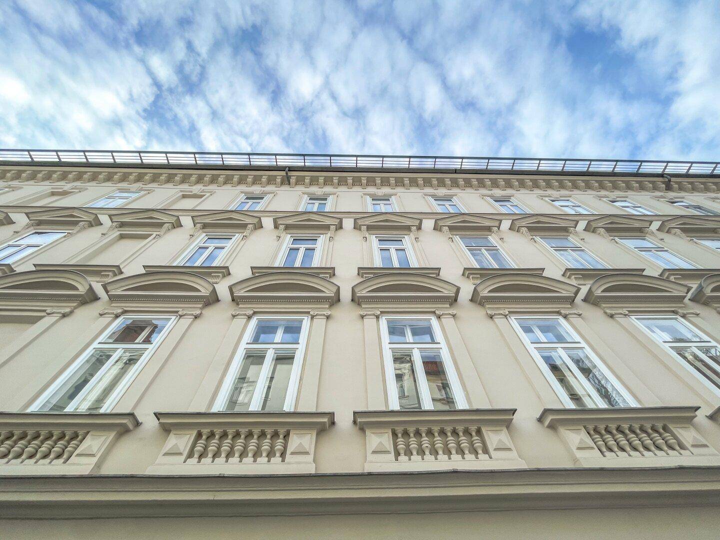 Detailansicht der oberen Etagen eines historischen Gebäudes mit reich verzierten Fenstern und blauem Himmel.
