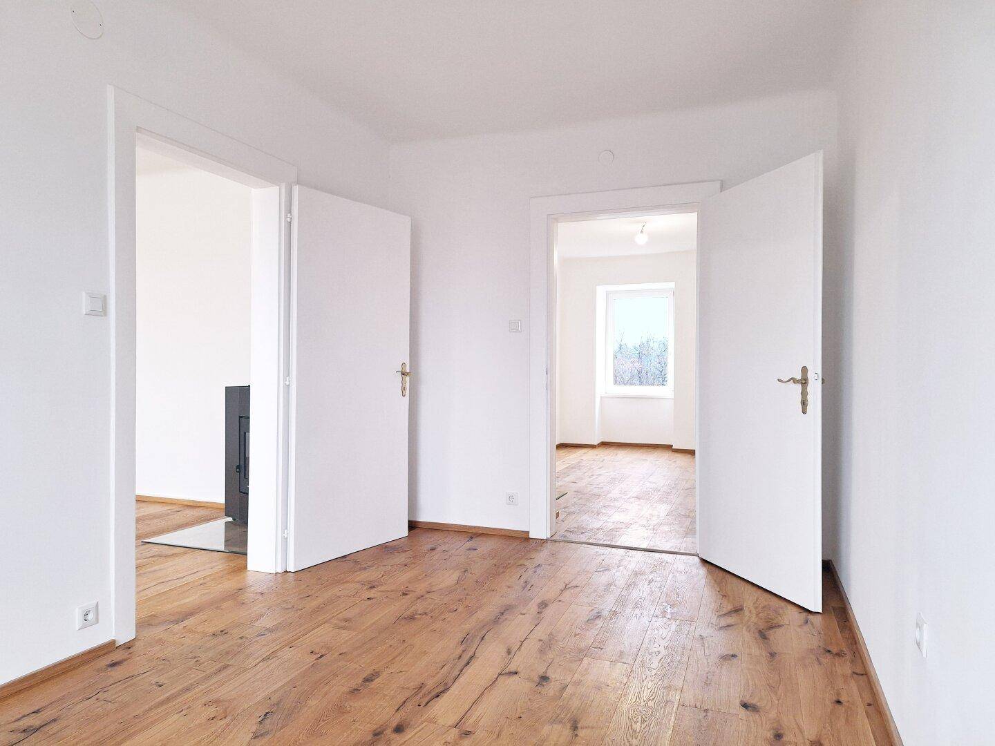 Heller Flur mit Holzboden und zwei offenen Türen, die zu weiteren Räumen führen.