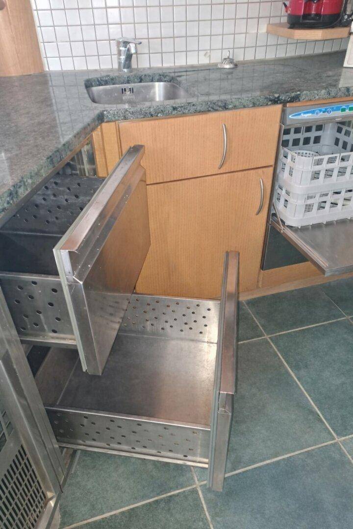 Detailansicht einer Küche mit Granitarbeitsplatte, Spülbecken und ausziehbaren Metallschubladen.