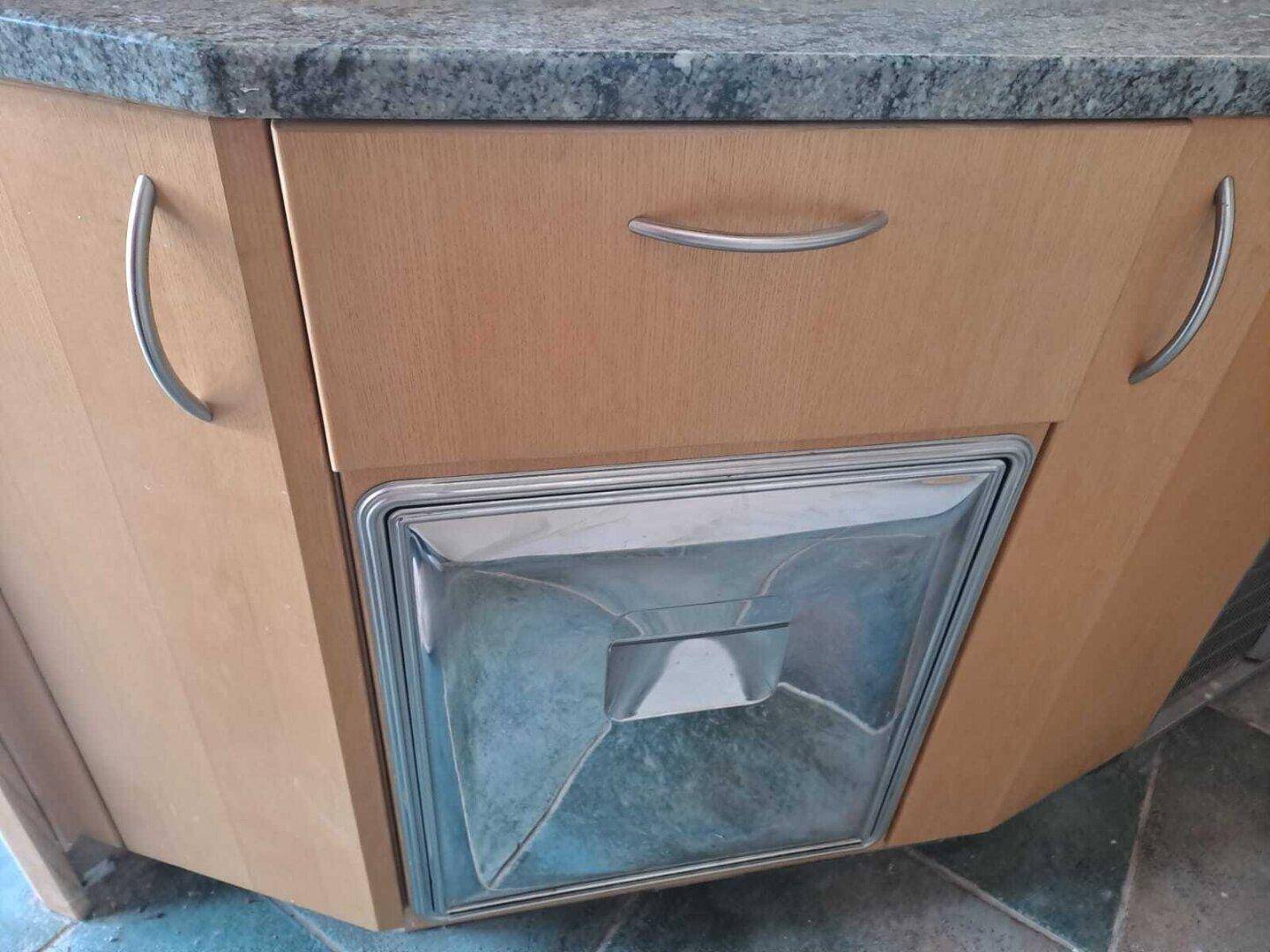 Detailaufnahme eines integrierten Küchengeräts mit Metallfront und Holzschränken.