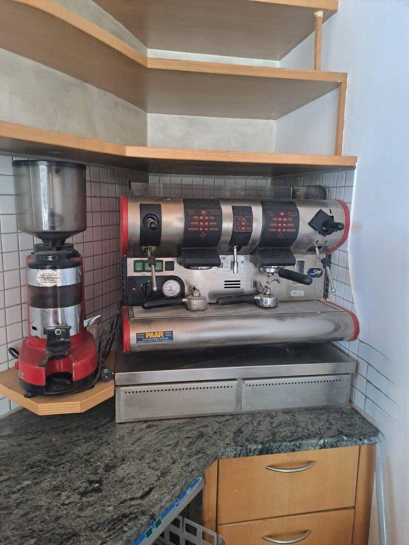 Professionelle Kaffeemaschine und Kaffeemühle auf einer Granitarbeitsplatte mit Holzregalen.