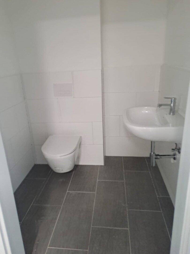 Ein kleines, modernes Gäste-WC mit weißen Wandfliesen und dunklem Fliesenboden.