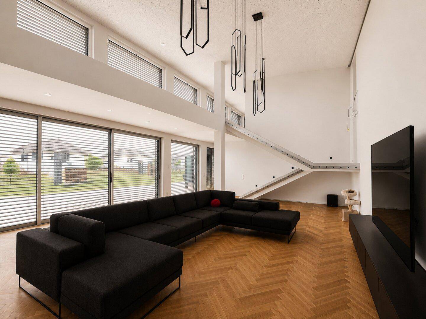 Großzügiges Wohnzimmer mit hoher Decke, Fischgrätparkett und großer Eckcouch für entspannte Stunden.