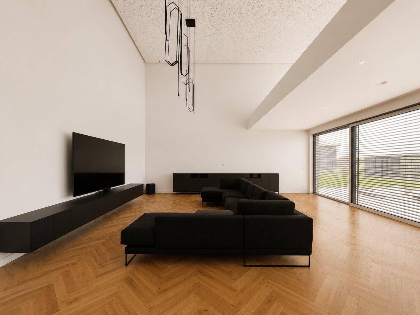 Weitläufiges Wohnzimmer mit minimalistischer Einrichtung, hohen Decken und viel Tageslicht durch die Fensterfront.