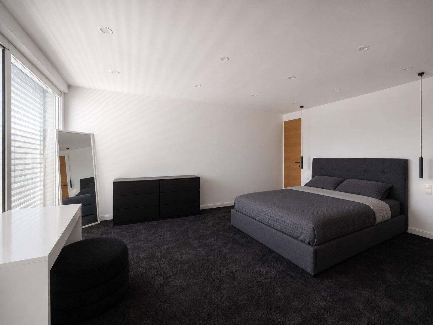 Geräumiges Schlafzimmer mit großem Doppelbett, dunklem Teppich und viel Tageslicht durch die Fenster.