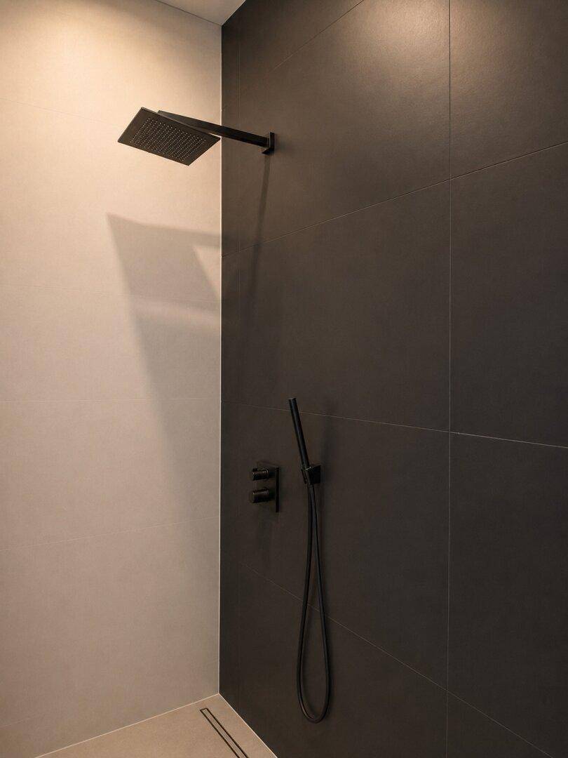Moderne Dusche mit schwarzen Armaturen und großformatigen dunklen Fliesen für ein elegantes Ambiente.
