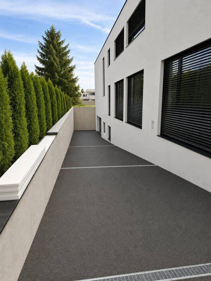 Moderne Gebäudefassade mit dunklen Fensterrahmen und gepflastertem Außenbereich.