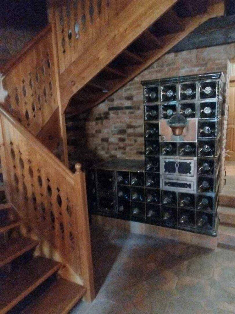 Traditioneller Kachelofen neben einer Holztreppe mit kunstvollen Schnitzereien im Flurbereich.