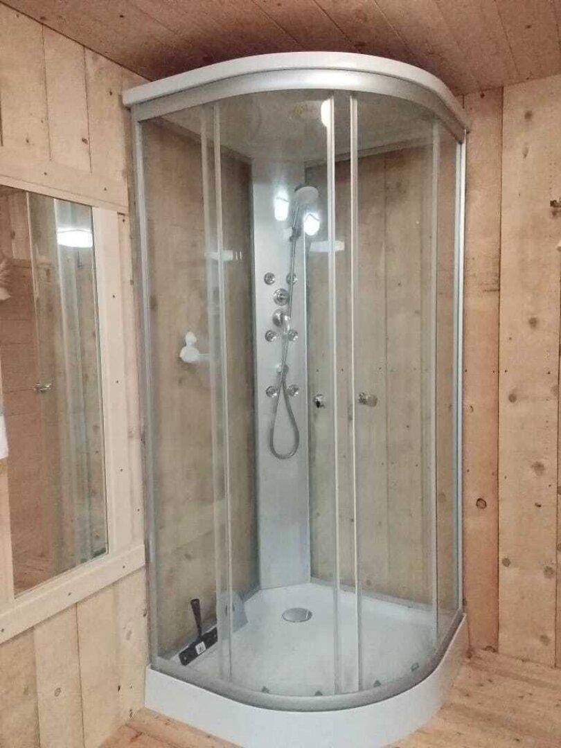 Duschkabine mit mehreren Duschköpfen und Holzverkleidung im Badezimmer.